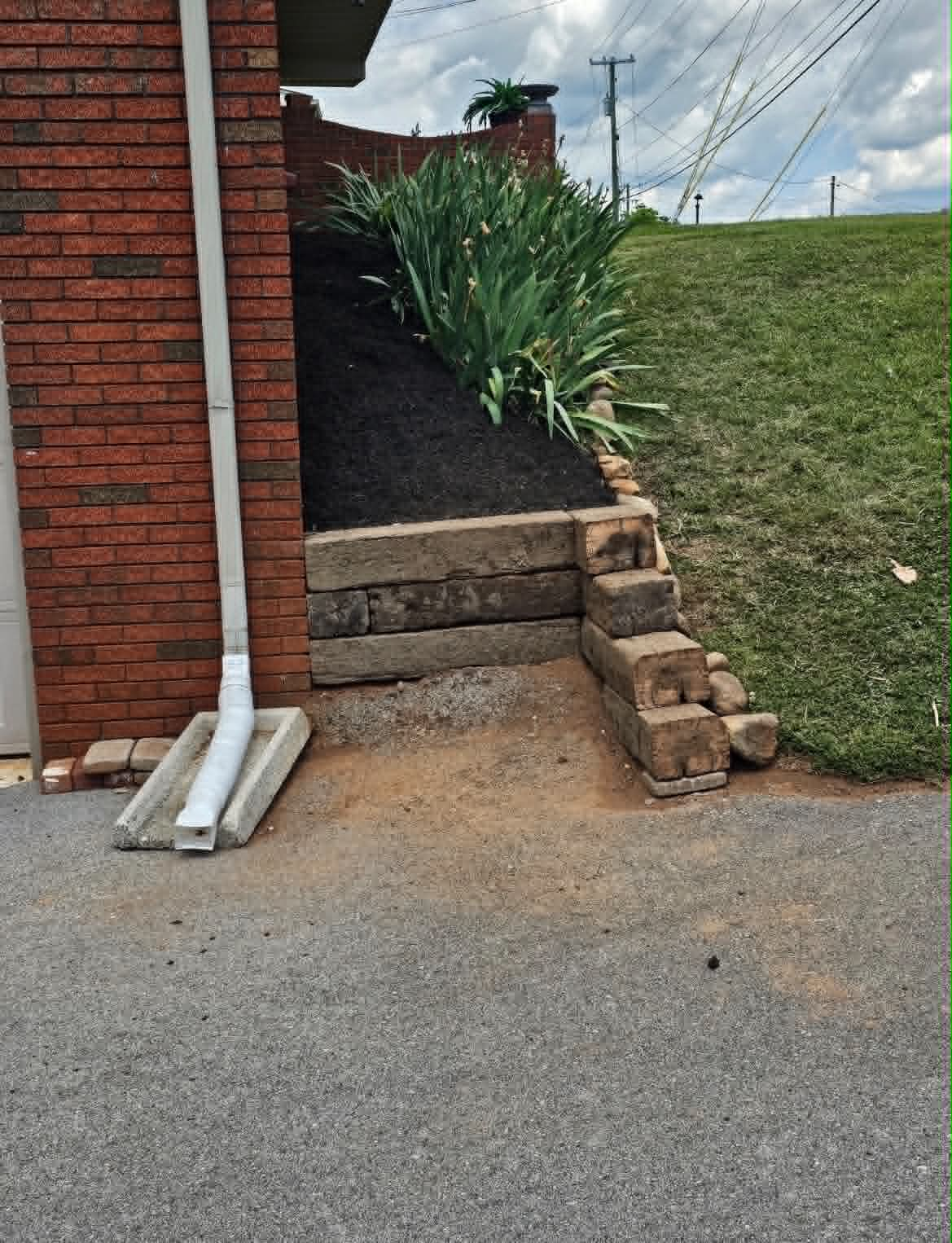 Finished retaining bed with fresh mulch and timber edging beside a brick home