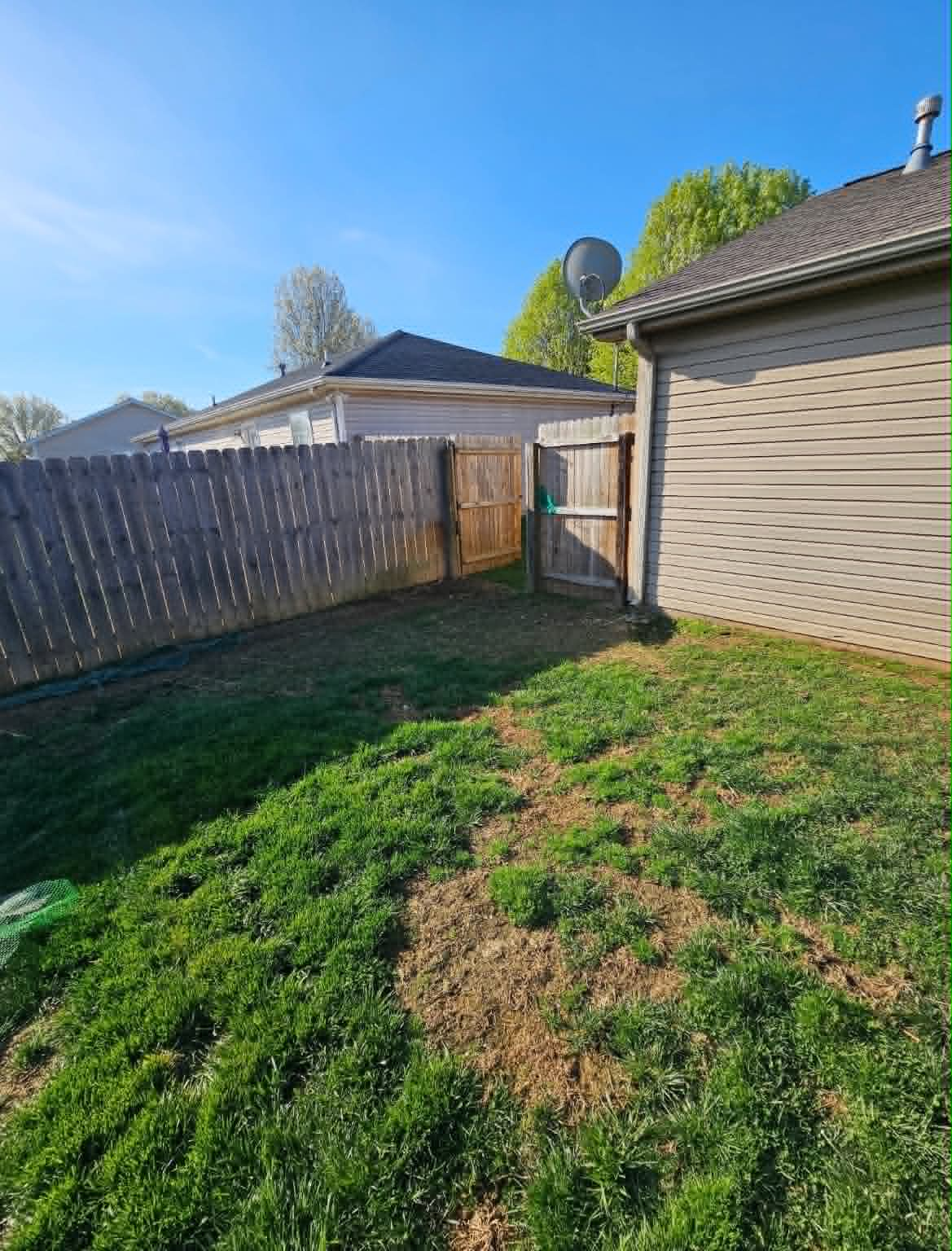 Side yard with patchy grass near a fence and gate