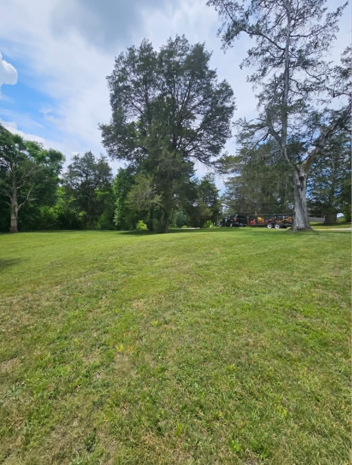 Freshly mowed open field with mature trees and equipment trailer