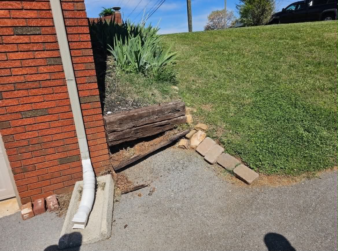 Before view of a sloped flower bed beside a brick home